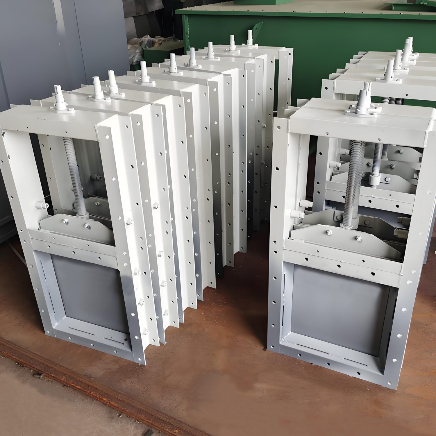 Varias cajas metálicas con agujeros y tornillos en la parte superior, diseñadas para un mecanismo de válvula de compuerta deslizante.