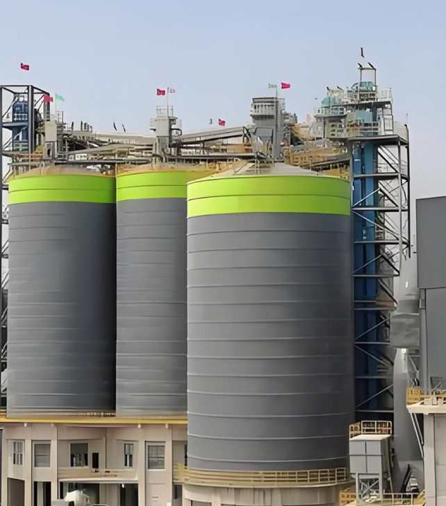 A large cement silo in an industrial setting, showcasing its height and connection to the cement processing equipment
