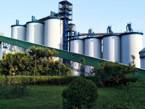 A large cement plant featuring multiple towering silos against a clear sky.